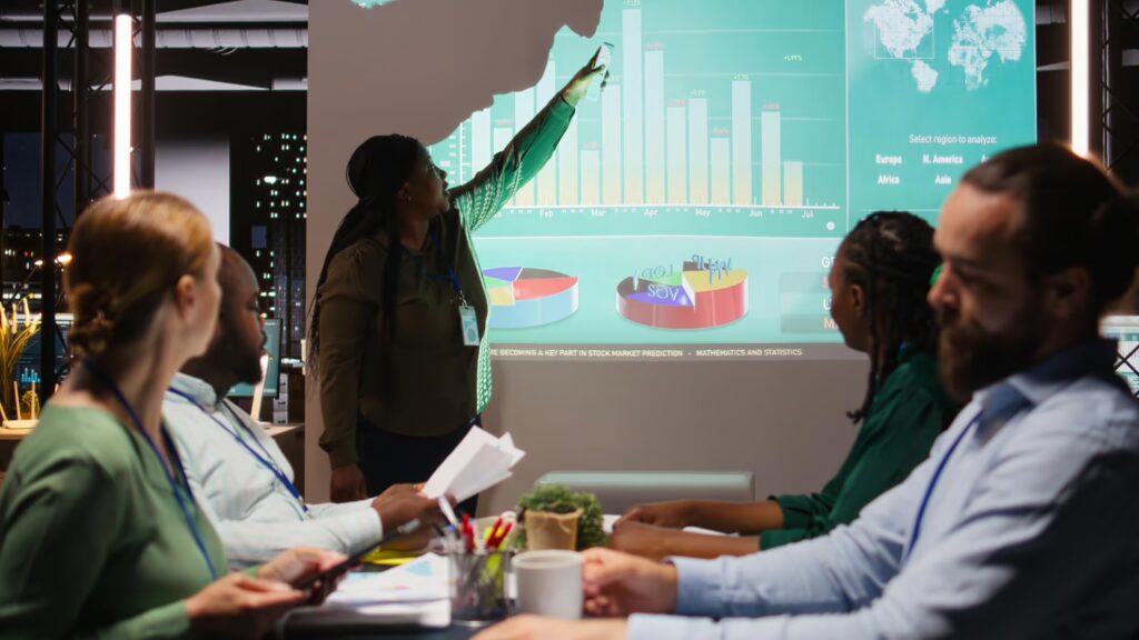 image of people at the table discussing business. A projector also showing data on the wall.